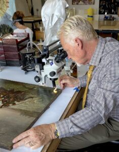 a white man looks into a microscope to evaluate a painting's condition